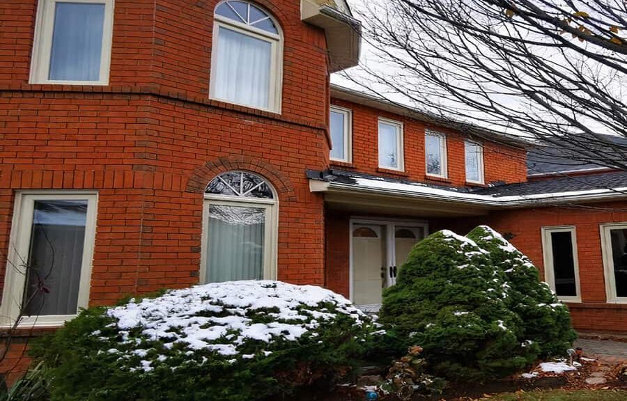 Red brick house with snowy shrubs.